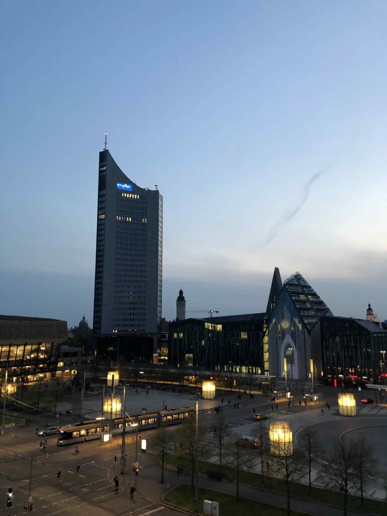 Abendlicher Blick auf den Augustusplatz in Leipzig mit beleuchteter Universität, Hochhaus und Straßenbahnverkehr während der After Work Party.